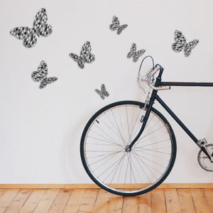 Sticker décoratif mural papillons en 3D modèle à triangles noirs et gris collés dans une pièce avec un vélo